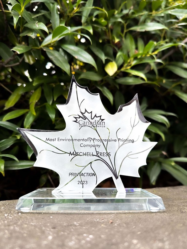 Mitchell Press Award for Most Environmental Progressive Printing Company from the Canadian Printing Awards 2023. Leaf shaped award is standing on concrete ground with leaves in background.